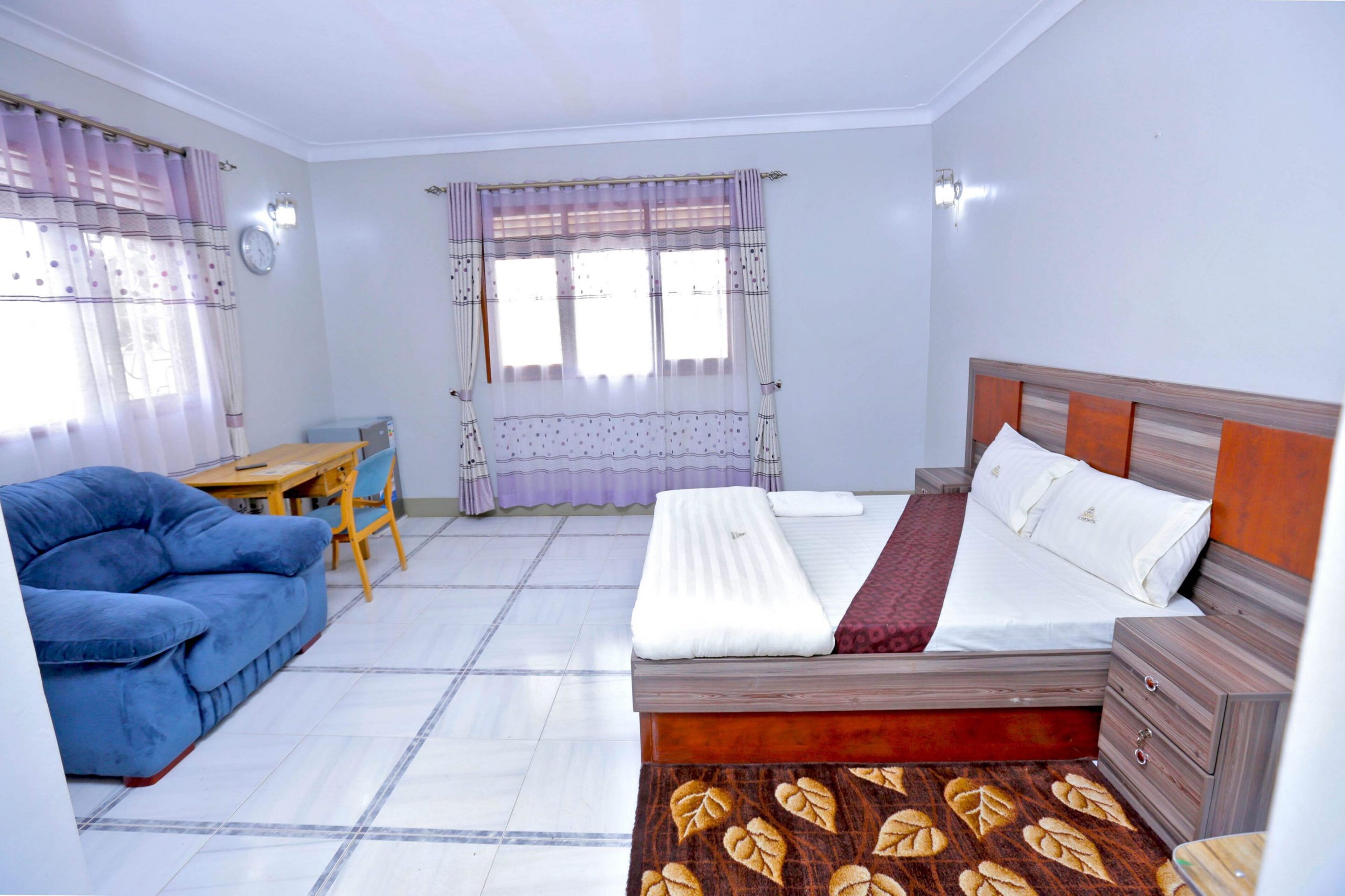 Un dormitorio con una cama, un sofá azul, una mesa de madera y un tapete estampado.