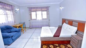 Un dormitorio con una cama, un sofá azul, una mesa de madera y un tapete estampado.