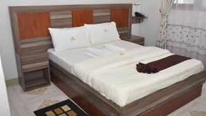 A neatly made bed with white linens and a brown throw blanket, a wooden headboard, and a bedside table with a lamp.