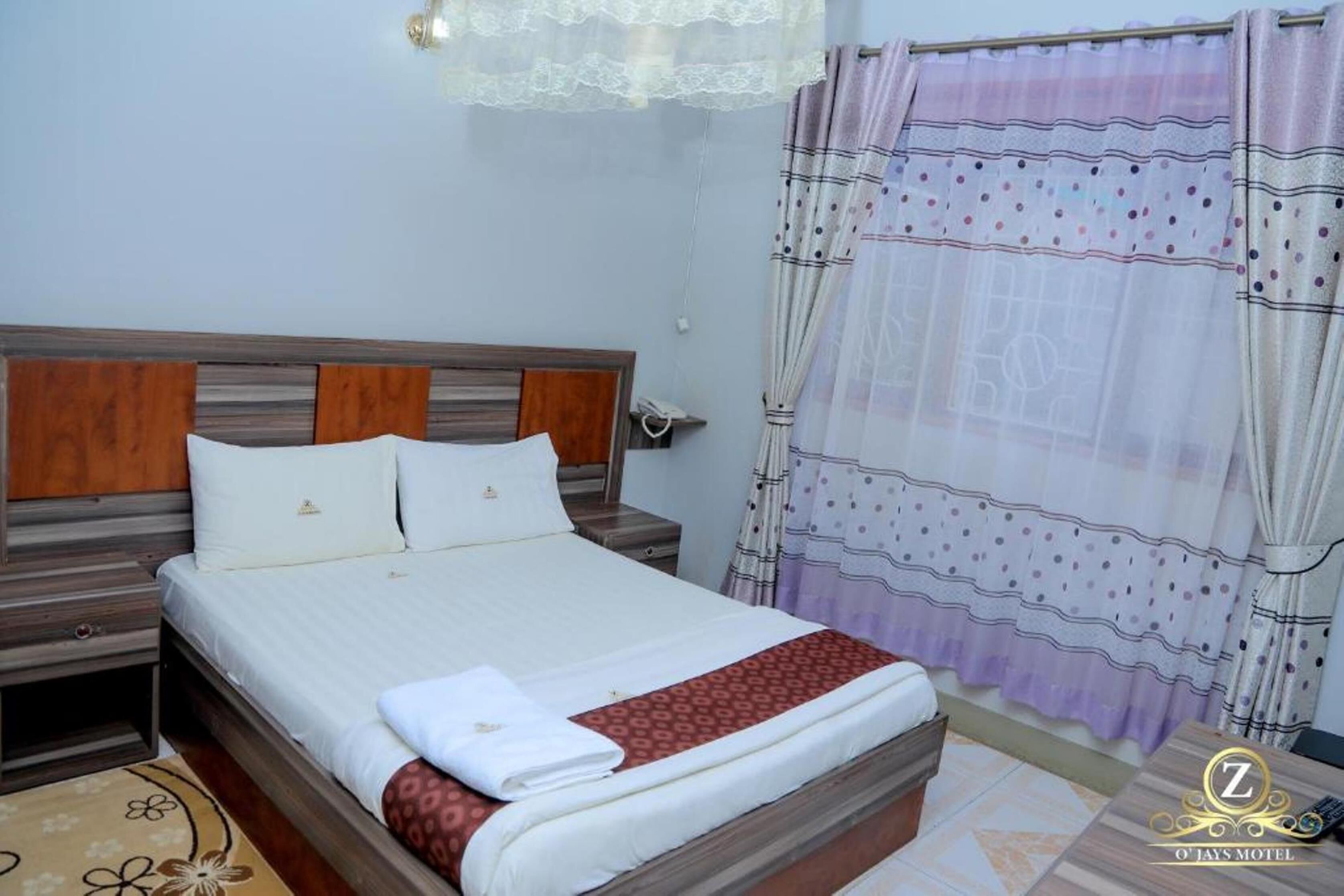 A neatly made bed with a wooden headboard, a bedside table, and a patterned rug.