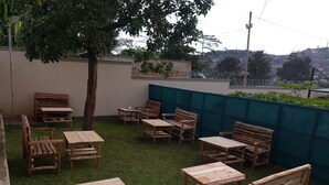 An outdoor seating area with wooden tables and chairs, a tree, and a view of a hillside.