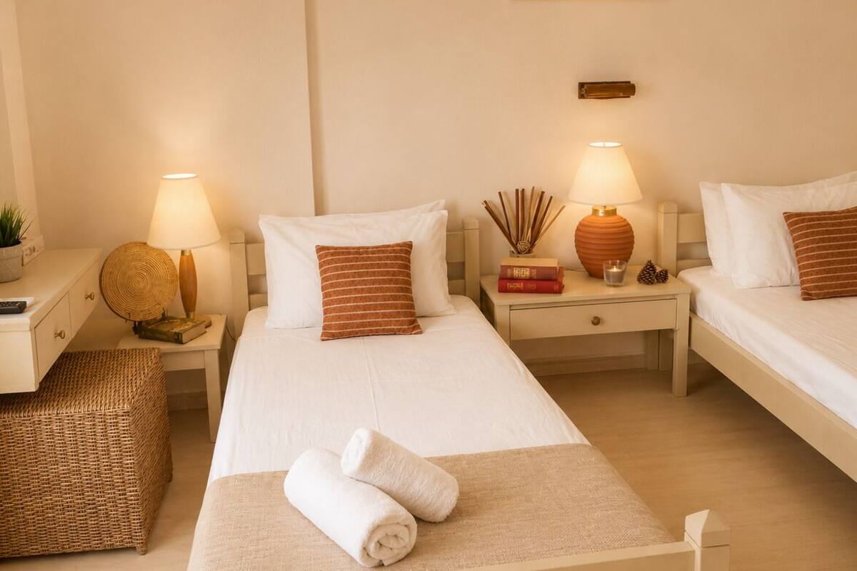A hotel room with two beds, bedside tables, lamps, a small rug, and a wall-mounted picture.