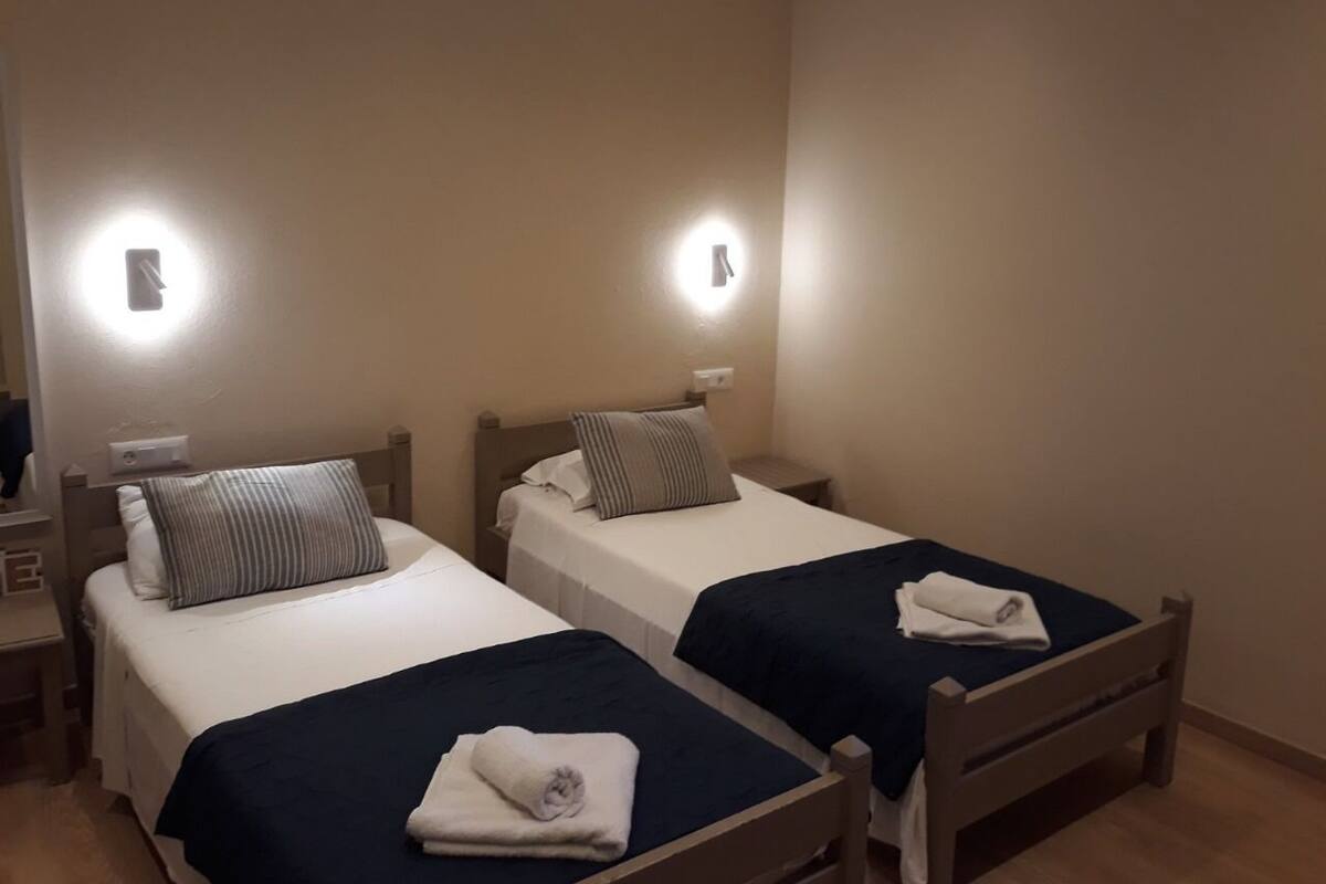 Two single beds with headboards, bedside tables, and wall-mounted lights in a room.