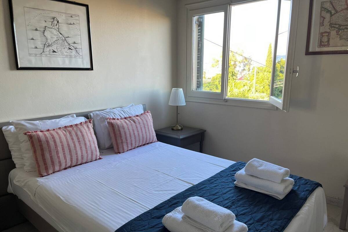 A neatly made bed with white and pink striped pillows, a blue quilt, and folded towels.