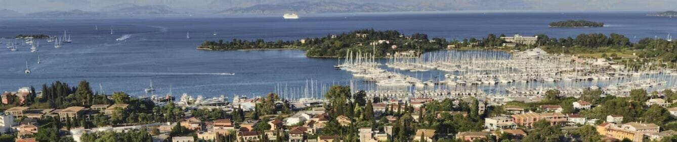 A coastal town with a marina filled with boats, surrounded by residential buildings and greenery.
