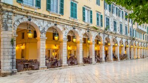 A row of outdoor cafe tables and chairs under a covered walkway with stone arches and hanging lanterns. - Pierhouse Hotel Corfu - Gouvia (Gouvia)