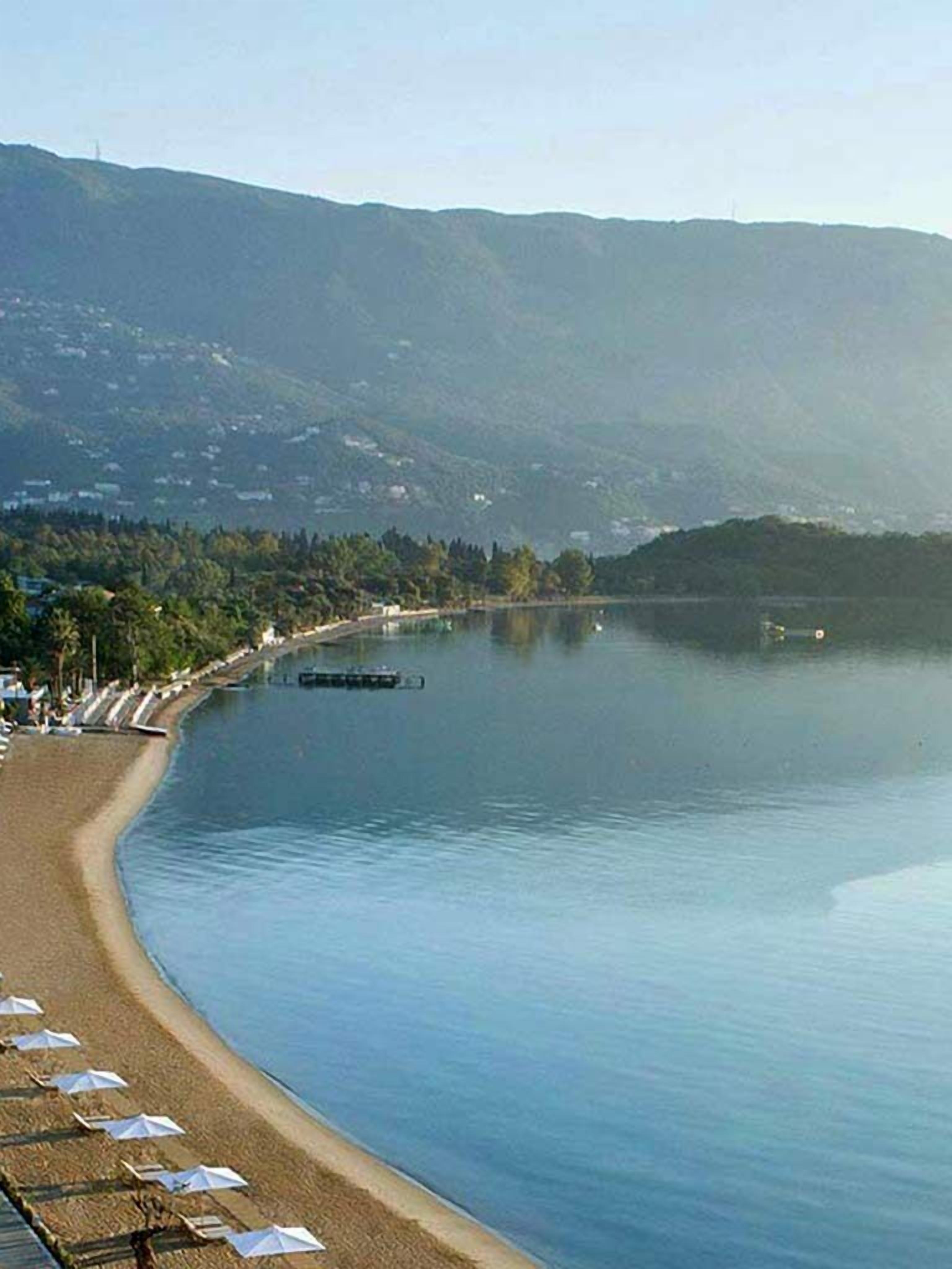 Una playa con sombrillas y un lago tranquilo, rodeada de colinas.