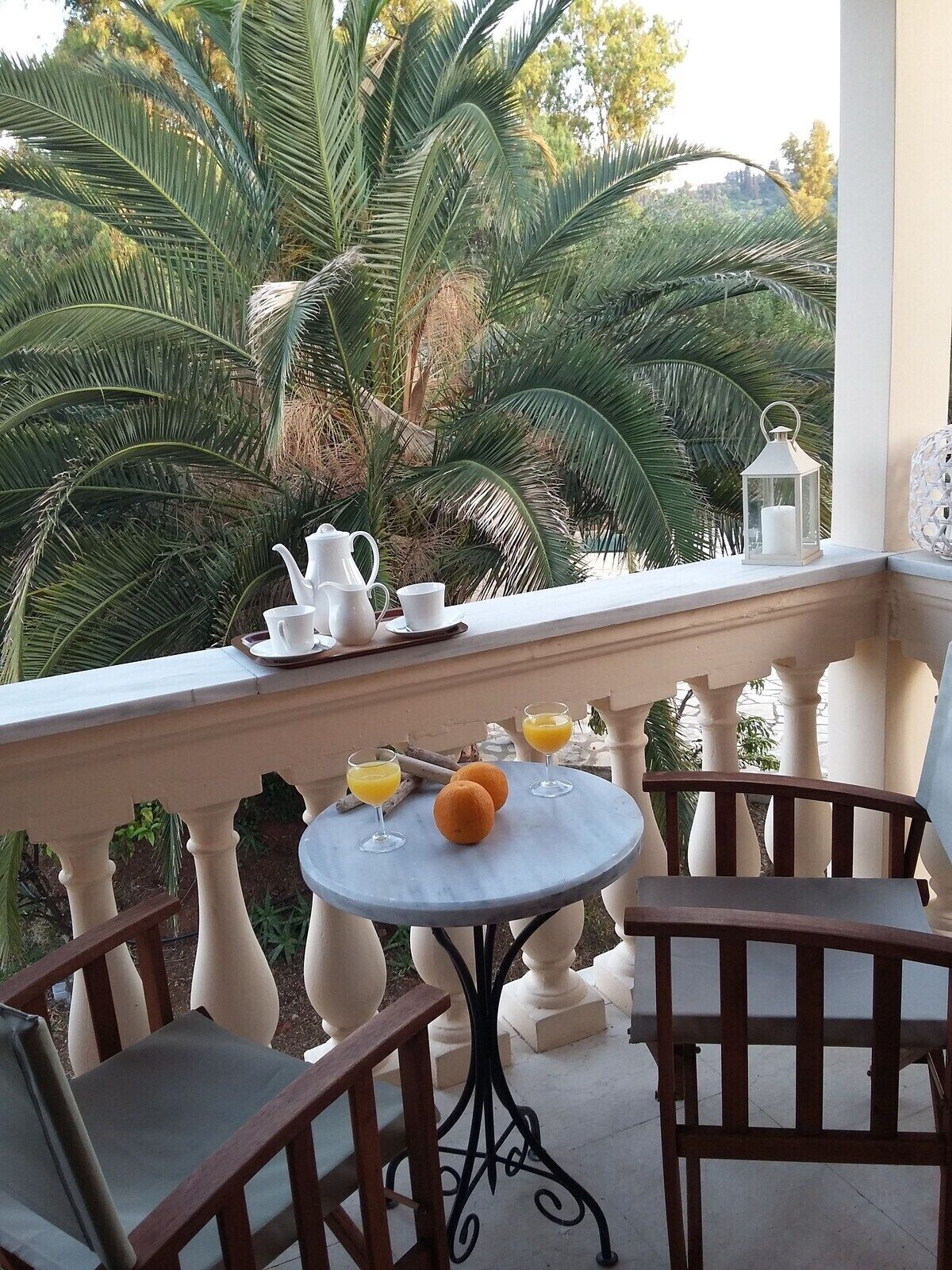 A balcony with a table set for two, featuring a white pitcher, cups, and glasses of orange juice, with a lantern and a decorative item on the railing.