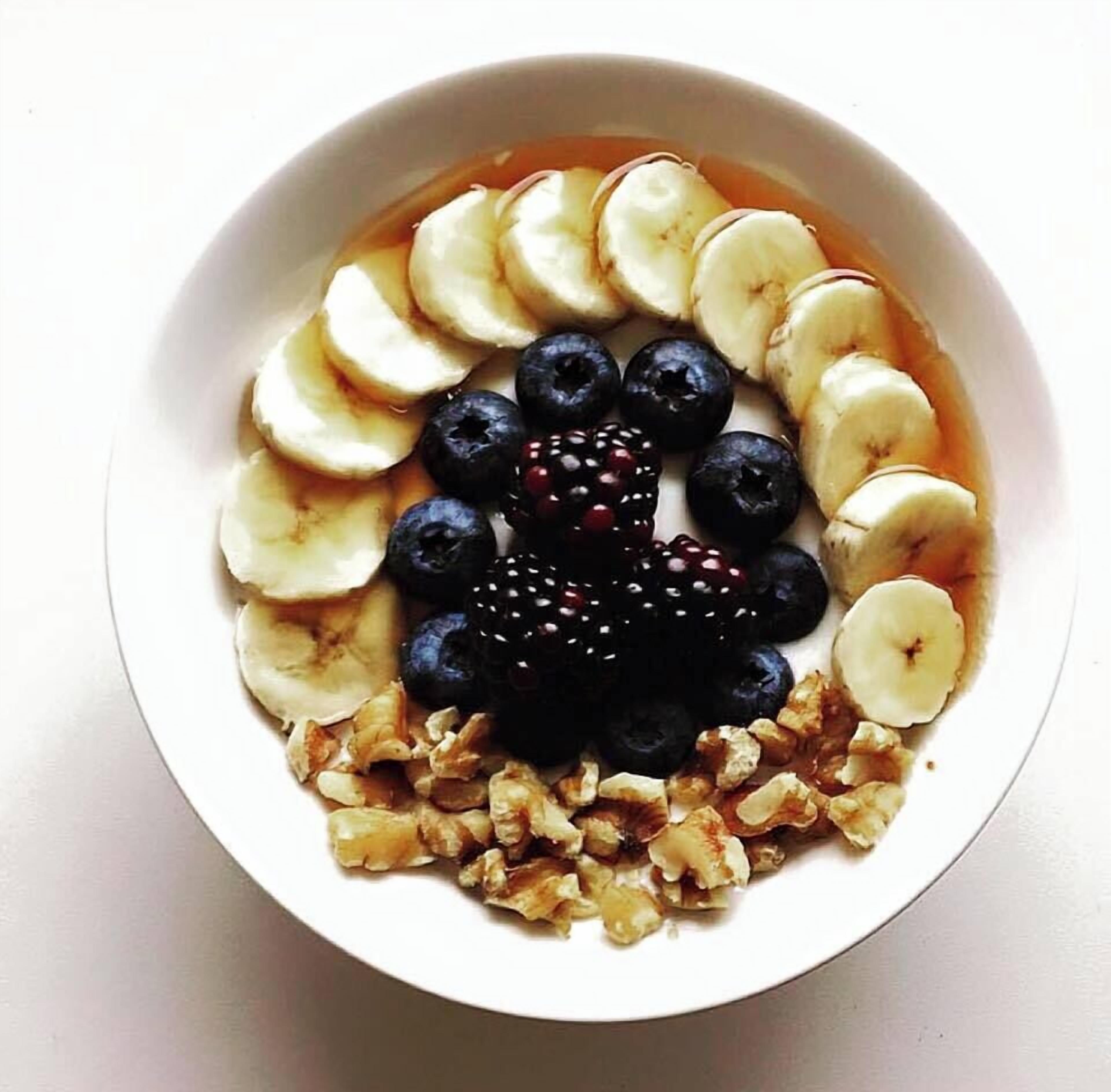 A bowl of sliced bananas, blueberries, blackberries, and walnuts.