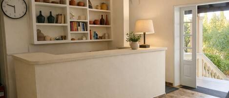 A reception area with a white counter, shelves with pottery and books, a clock, and a lamp.