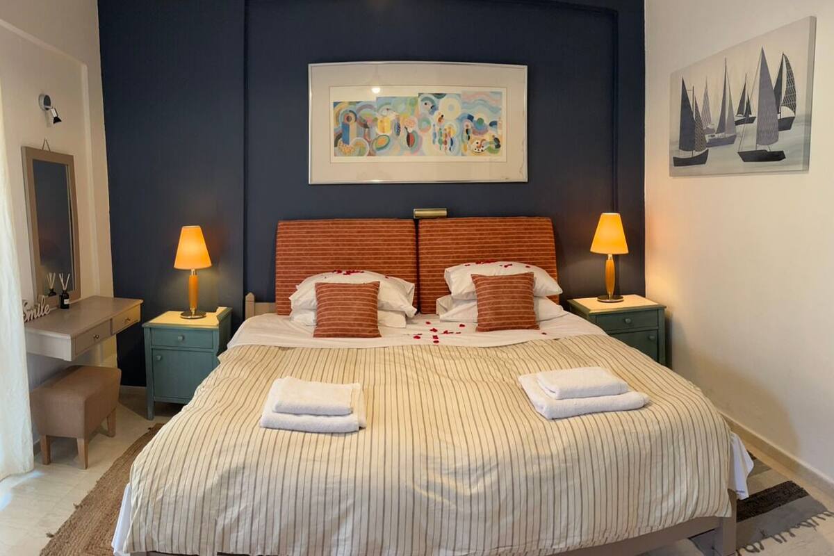 A hotel room with a bed, two nightstands, a desk, a chair, and artwork on the walls.