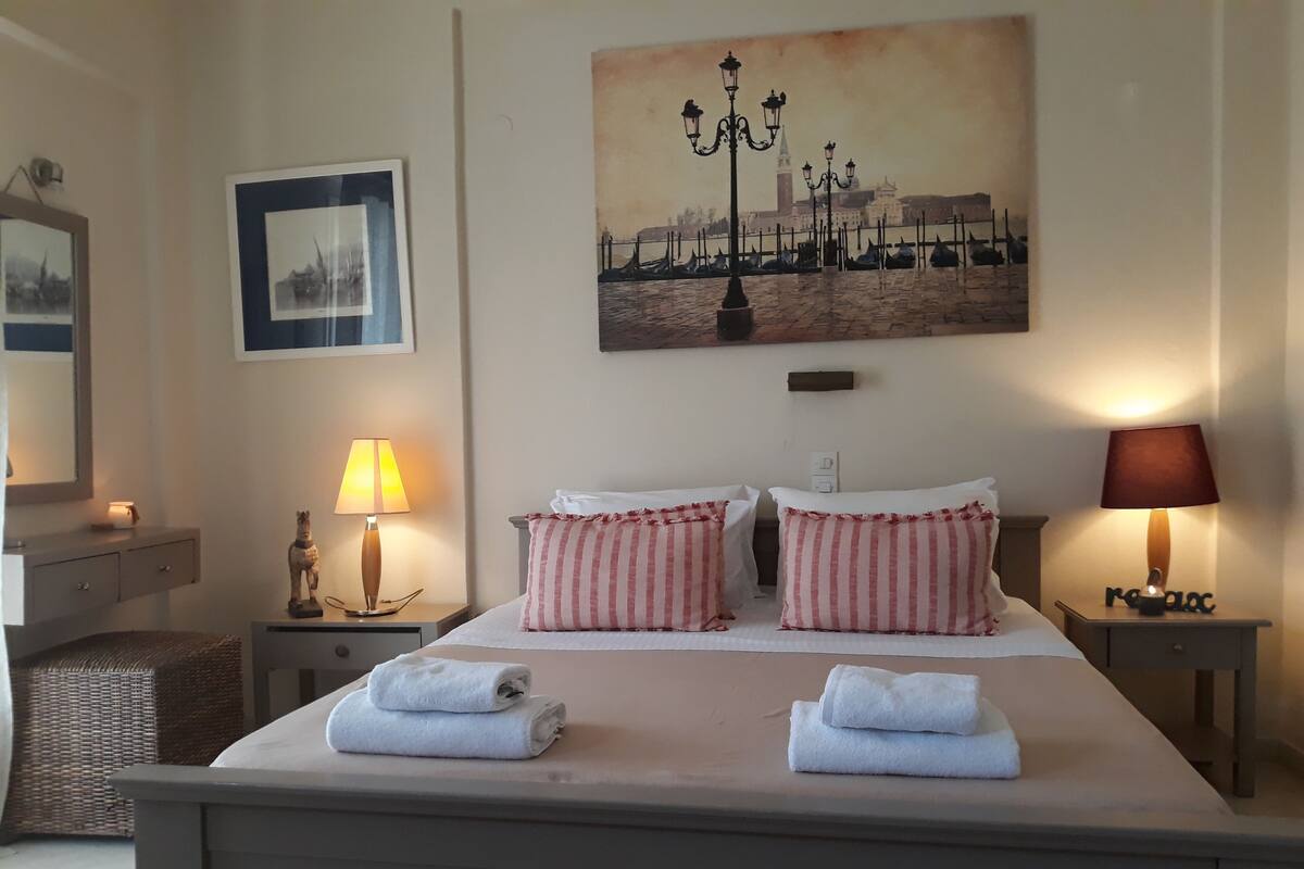 A hotel room with a bed, two bedside lamps, a nightstand, a wall-mounted lamp, a framed picture, and a painting.