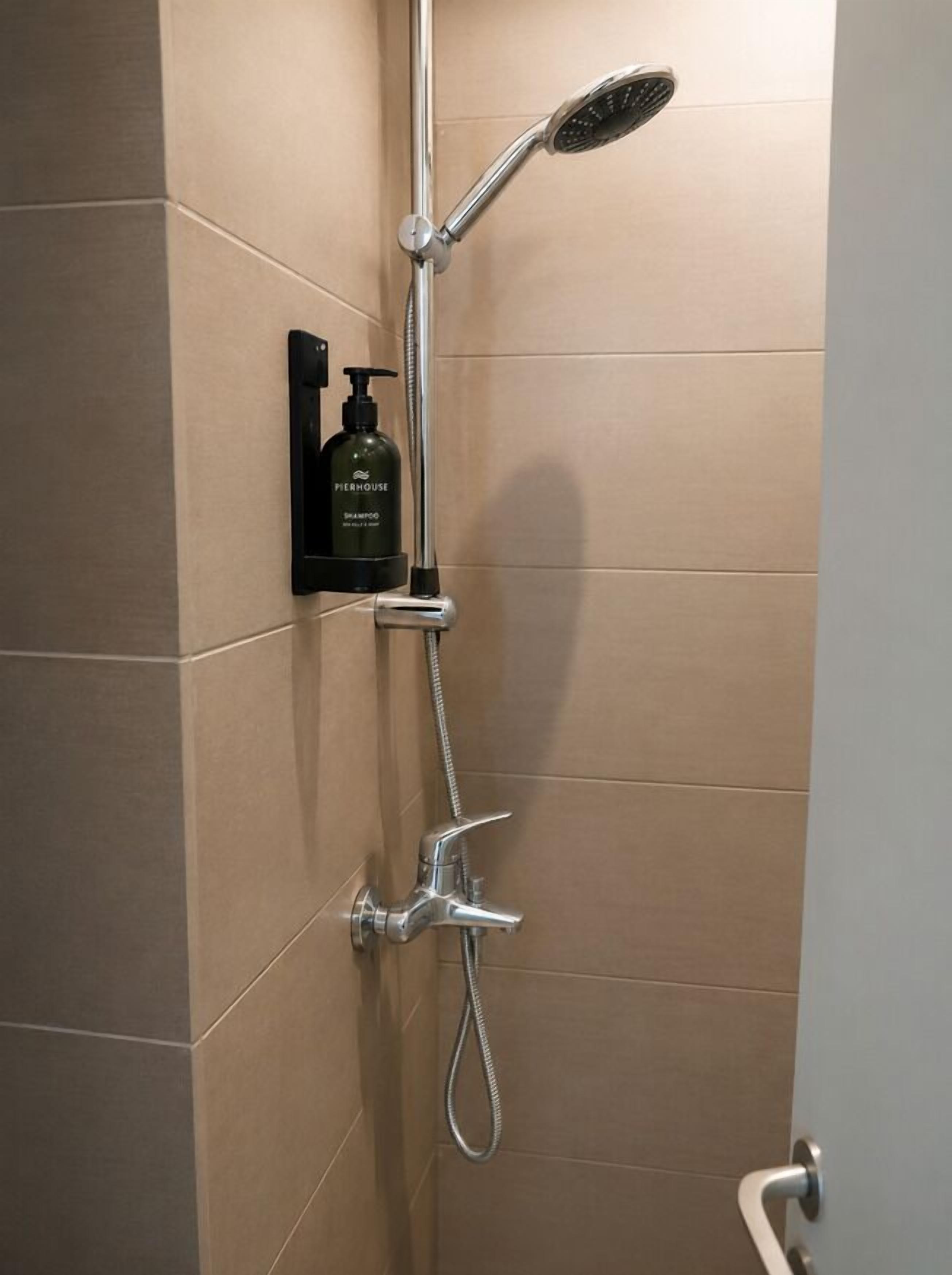 A shower with a handheld showerhead, a wall-mounted faucet, and a bottle of shampoo.
