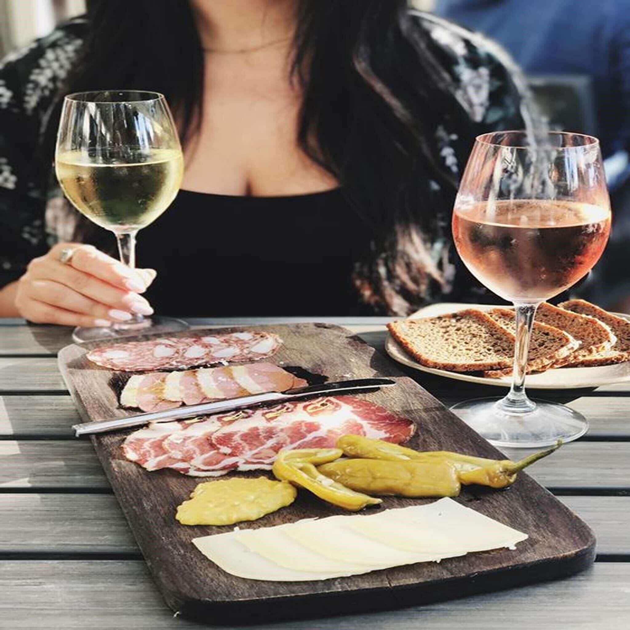 A dining table with a charcuterie board, two glasses of wine, and a person sitting in the background.