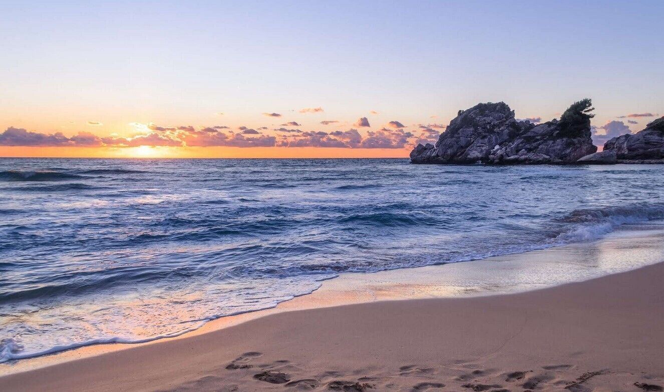 A beach with waves, a sunset, and rocky formations.