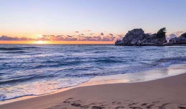 A beach with waves, a sunset, and rocky formations.