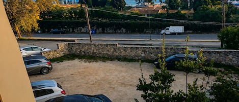 A parking area with several cars, a stone wall, and a view of a road with vehicles and trees in the background.