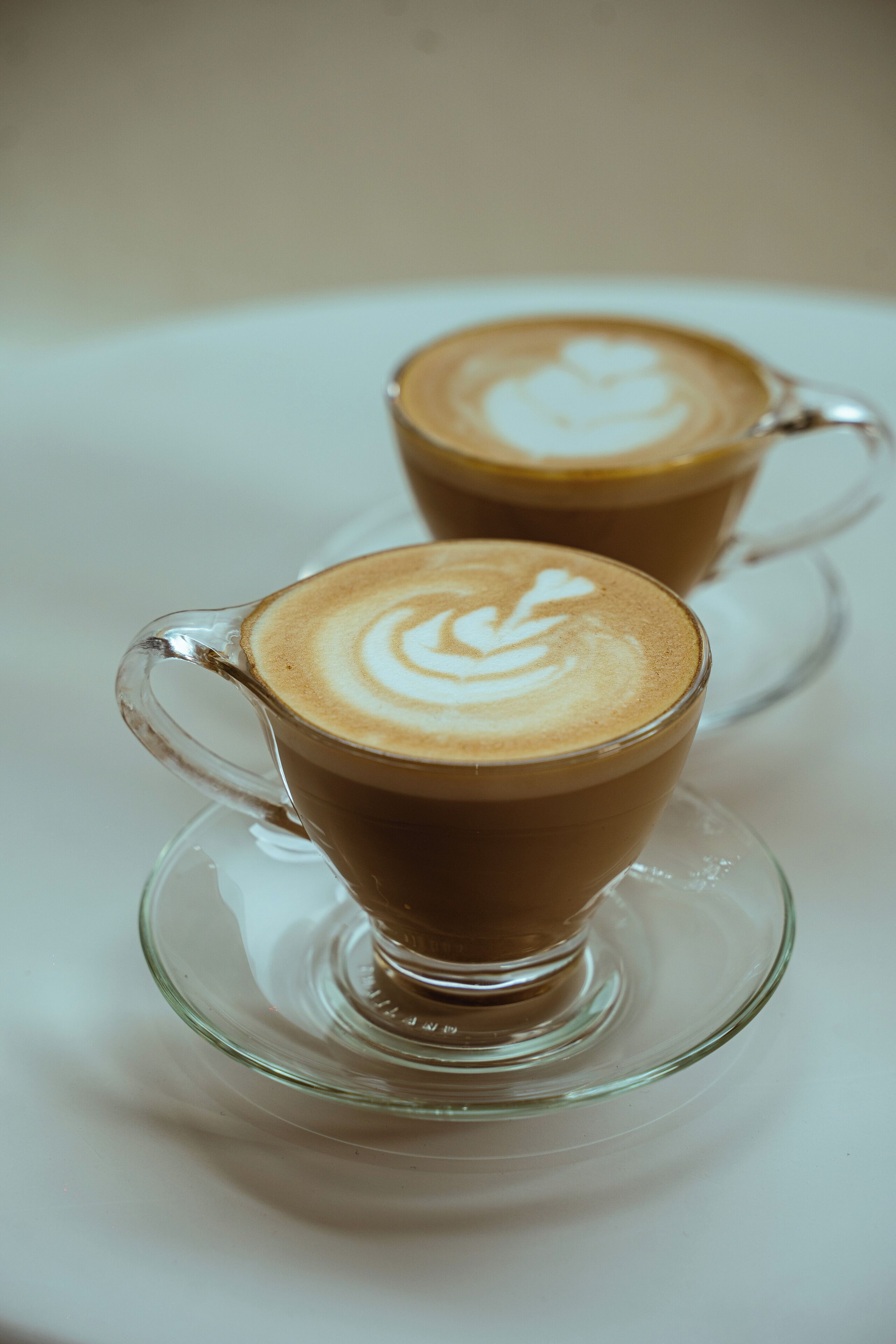 Duas chávenas de vidro transparentes com arte de latte sobre uma superfície branca.
