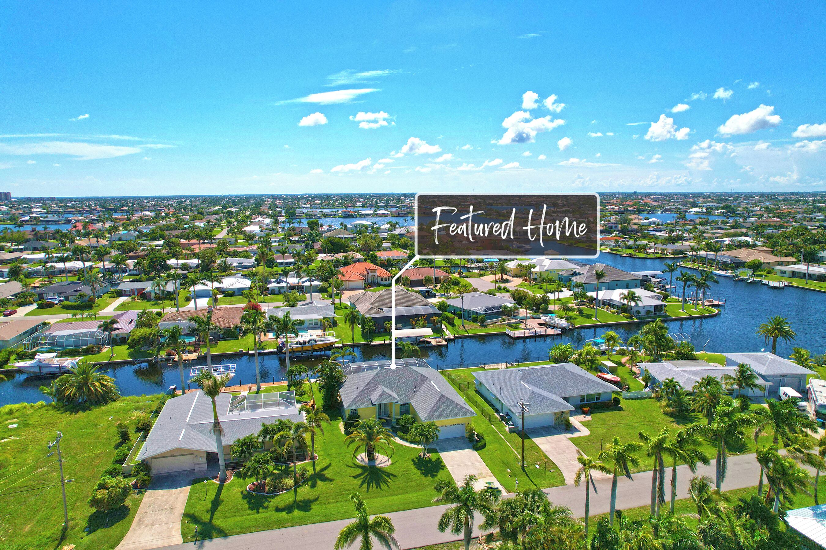 An aerial view of a residential area with houses, palm trees, and a body of water.