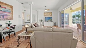A spacious living room with a beige sofa, a dining table with chairs, a TV, and a ceiling fan. - Cape Coral Waterfront Vacation Rental with Heated Pool and Boat Dock. (Cape Coral)