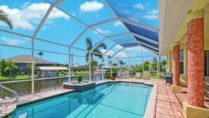 A swimming pool with a covered area, surrounded by palm trees and a clear sky. - Cape Coral Waterfront Vacation Rental with Heated Pool and Boat Dock. (Cape Coral)