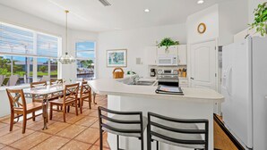 A modern kitchen with a central island, white cabinetry, and a dining area with wooden chairs. - Cape Coral Waterfront Vacation Rental with Heated Pool and Boat Dock. (Cape Coral)