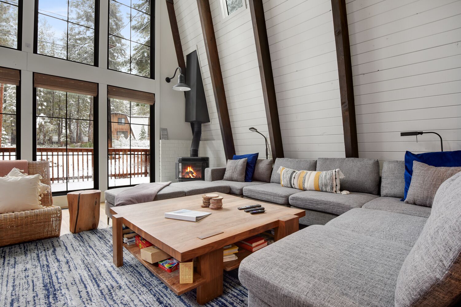 Una sala de estar acogedora con chimenea, un sofá, una mesa de centro y vistas a un paisaje nevado a través de grandes ventanales.