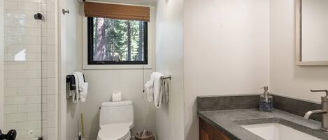 A bathroom with a toilet, a sink, a mirror, and a window with a view of trees.