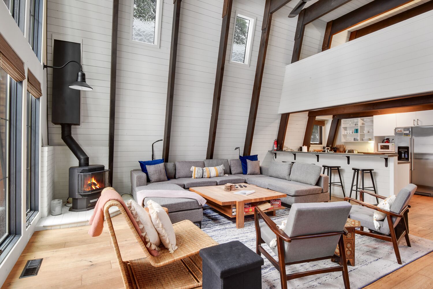 A cozy living room with a fireplace, a sofa set, a coffee table, and a kitchen area with stools.