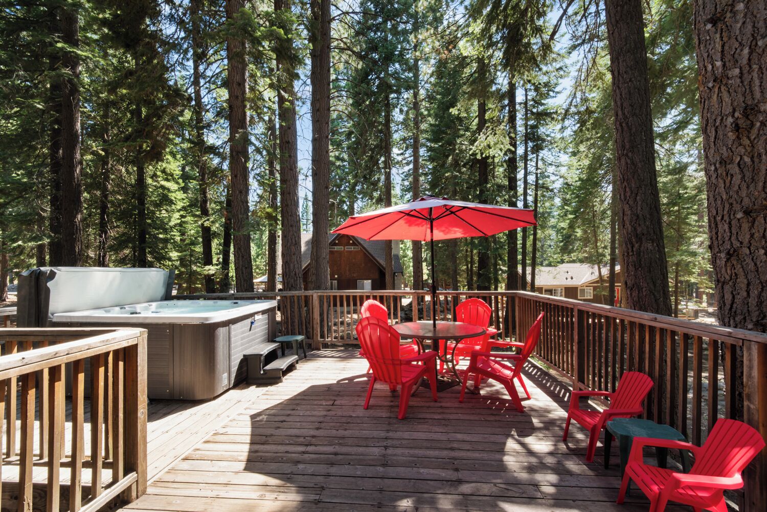 A wooden deck with a hot tub, red chairs, and a table with a red umbrella.