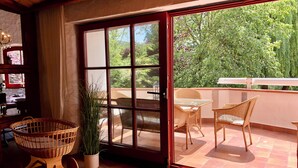 Une pièce dotée d’une porte-fenêtre coulissante donnant sur un patio extérieur aménagé avec des meubles en osier et un pot de fleurs.