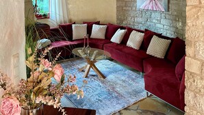 Un salon chaleureux avec un canapé en velours rouge, une table basse en verre et un mur en pierre.