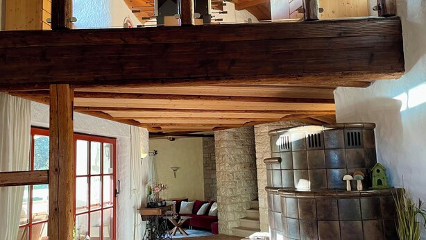 Un loft spacieux avec de hauts plafonds, des poutres apparentes, une cheminée en pierre et un coin salon confortable avec un canapé et une table.
