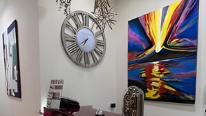 Un comptoir d’accueil avec une horloge, un tableau abstrait moderne et un élément décoratif mural.