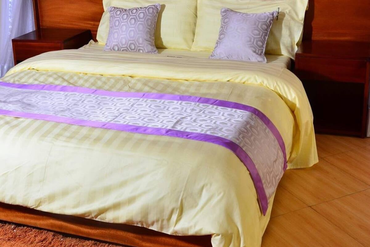 Una cama bien hecha con cabecera de madera, dos mesitas de noche y una colcha estampada.