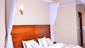 A bedroom with a wooden headboard, white bedding, and a canopy bed with white curtains. - Country Motel (Rubaare)