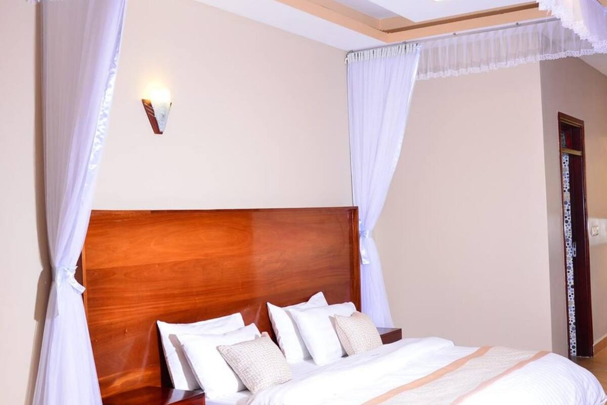 Un dormitorio con cabecera de madera, ropa de cama blanca y una cama con dosel y cortinas blancas.