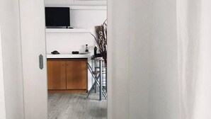 Un pasillo estrecho que conduce a una cocina con un armario de madera, una mesita y una silla.
