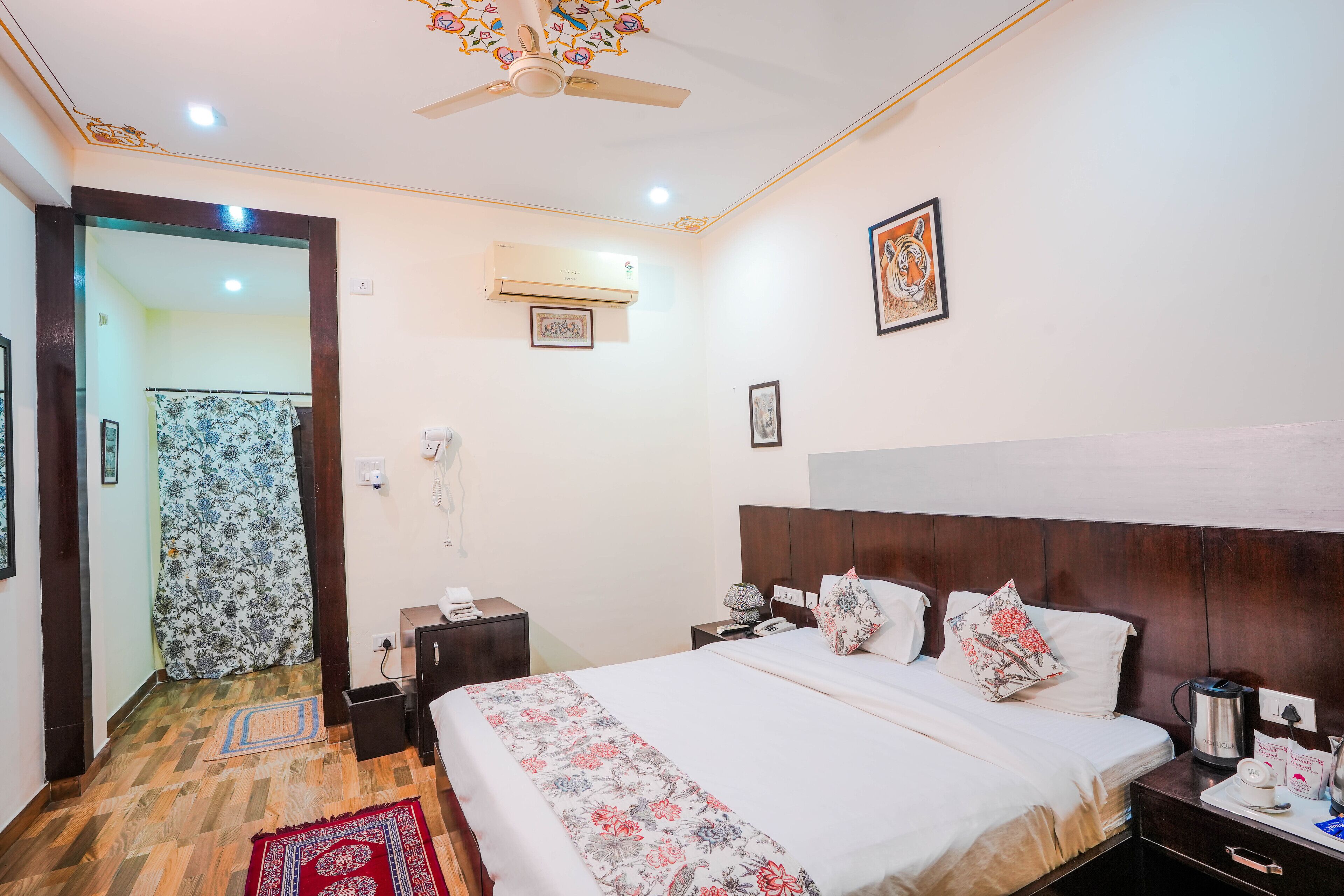 Habitación de hotel con cama, mesitas de noche, unidad de aire acondicionado, ventilador de techo y puerta que da a otra habitación.