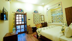 A bedroom with a bed, a chair, a small table, a mirror, and a window with curtains.