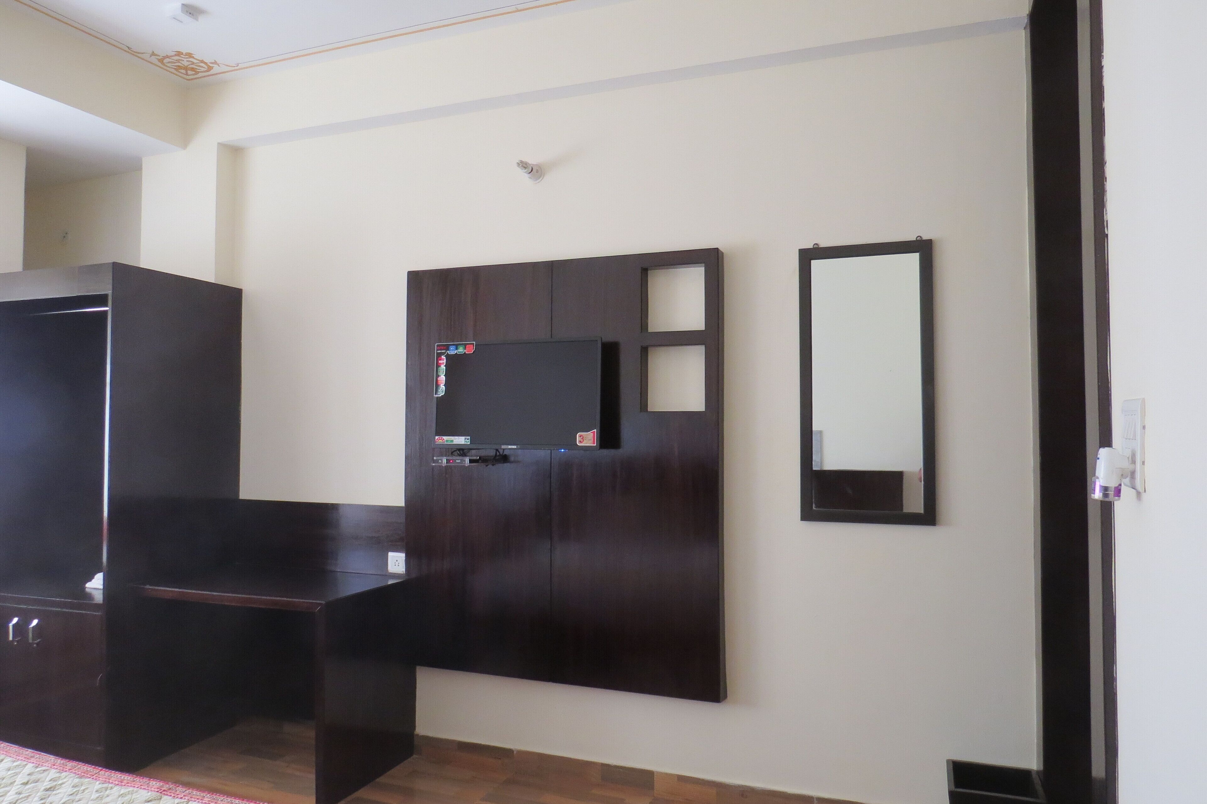 A room with a dark wooden wardrobe, a flat-screen TV mounted on a wall, and a mirror.