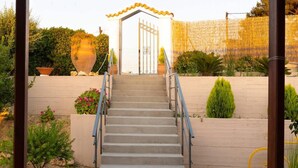 Un escalier menant à une entrée fermée par un portail, surmontée d’un toit décoratif, et entourée de plantes en pot et d’un mur en bois.
