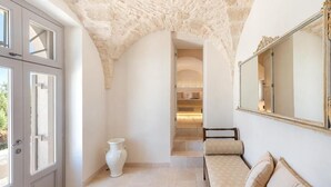 A room with a stone ceiling, a sofa with cushions, a large mirror, and a white vase on the floor. - Masseria Villa Verde (Fasano)