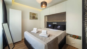 A modern hotel room with a neatly made bed, a bedside table with a clock and flowers, and a large mirror. - The Queen Villa Carlotta -21 (Luxembourg)