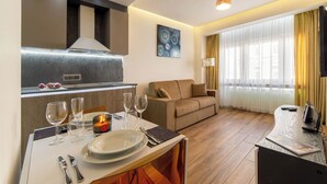 A modern living room with a sofa, a dining table set with plates and glasses, and a kitchen area with a stove and cabinets. - The Queen Villa Carlotta -21 (Luxembourg)