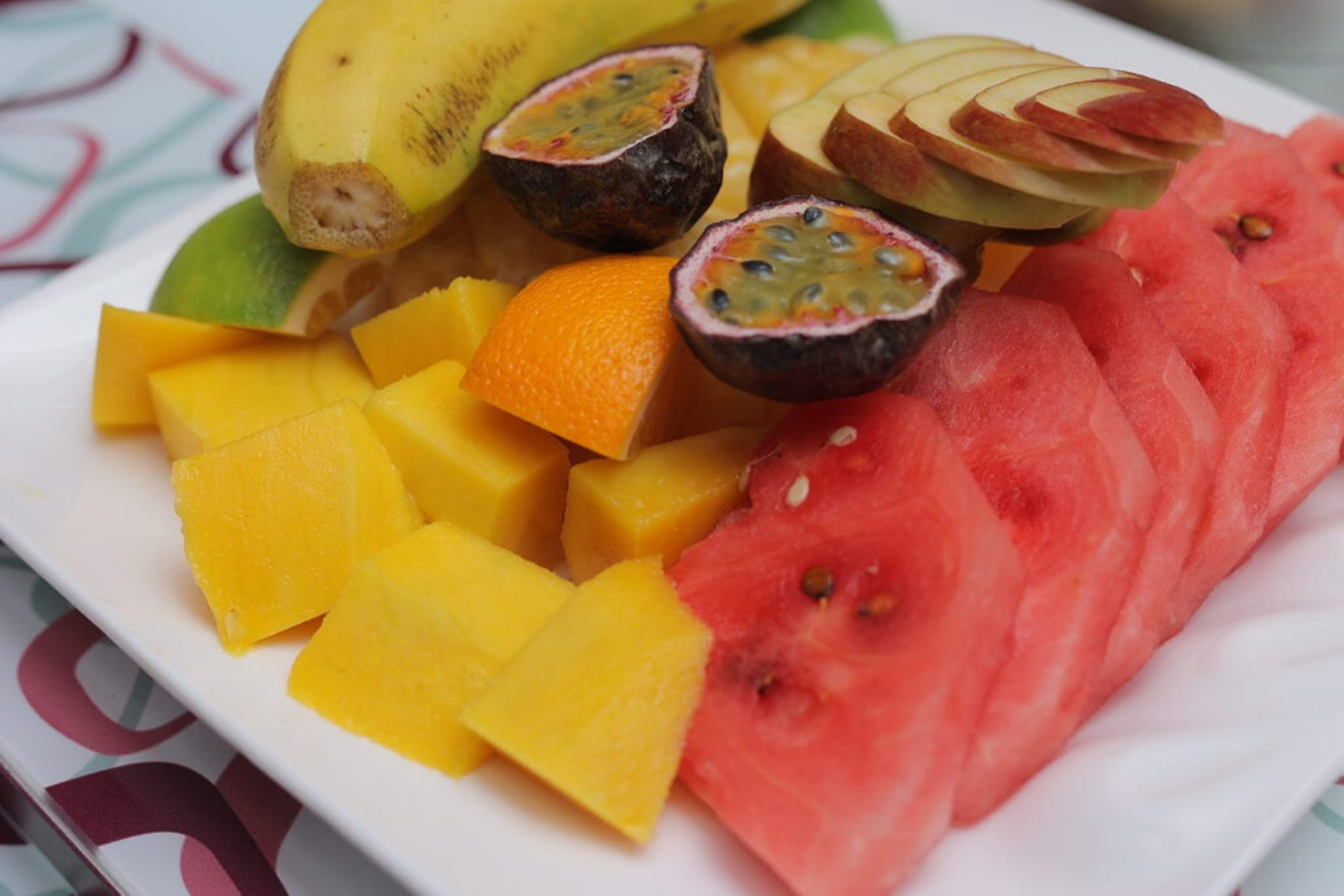 A plate of assorted fruits including watermelon, mango, passion fruit, and apple slices.