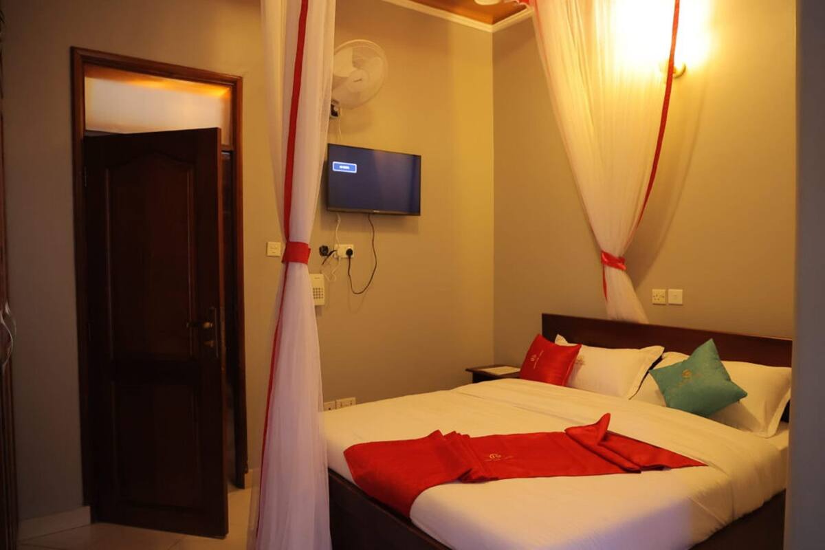 A hotel room with a bed, a television mounted on the wall, and a door.