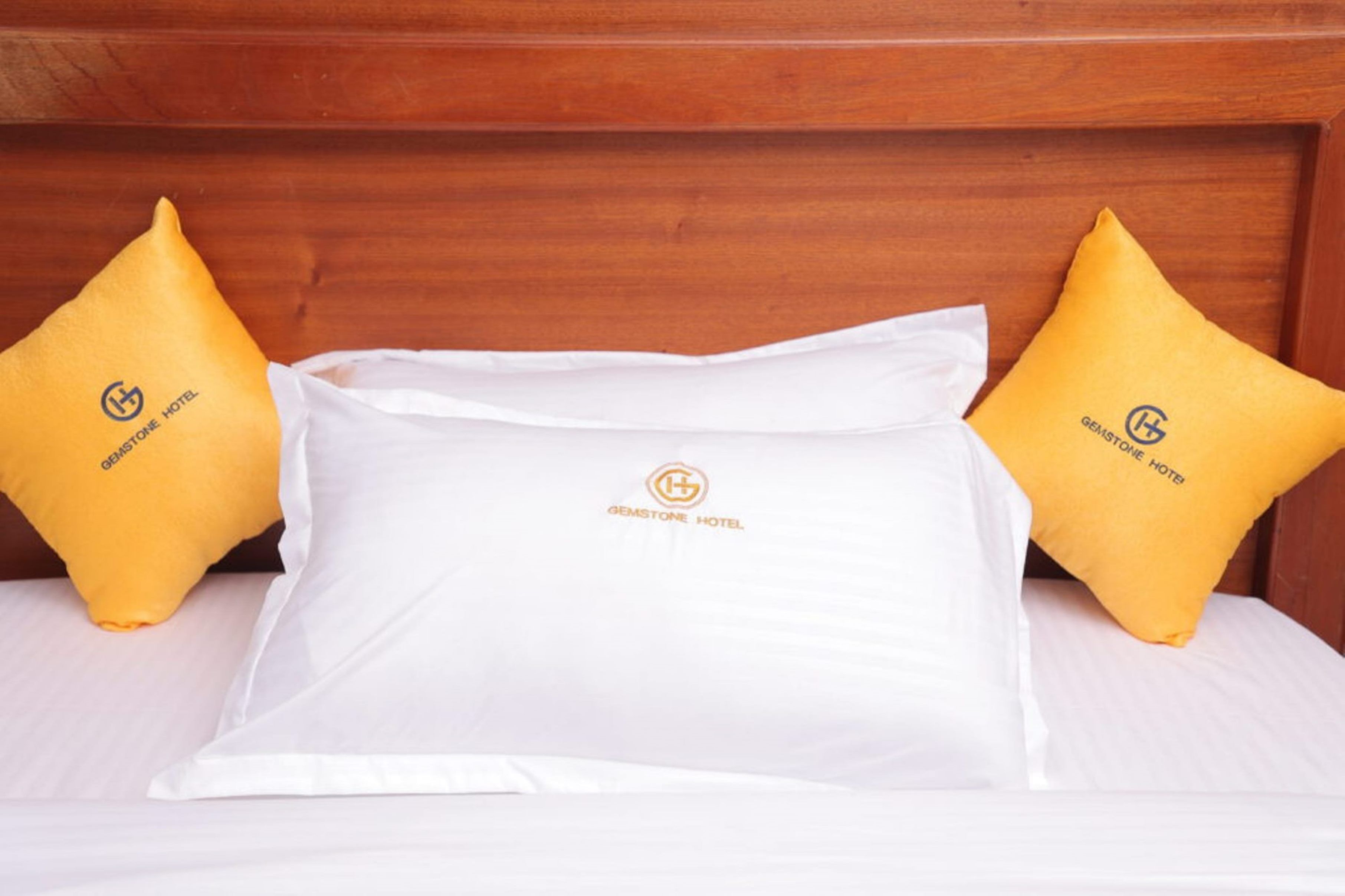 Una cama bien hecha con una almohada blanca y dos almohadas amarillas, cada una con el logotipo y nombre del Hotel Gemstone.