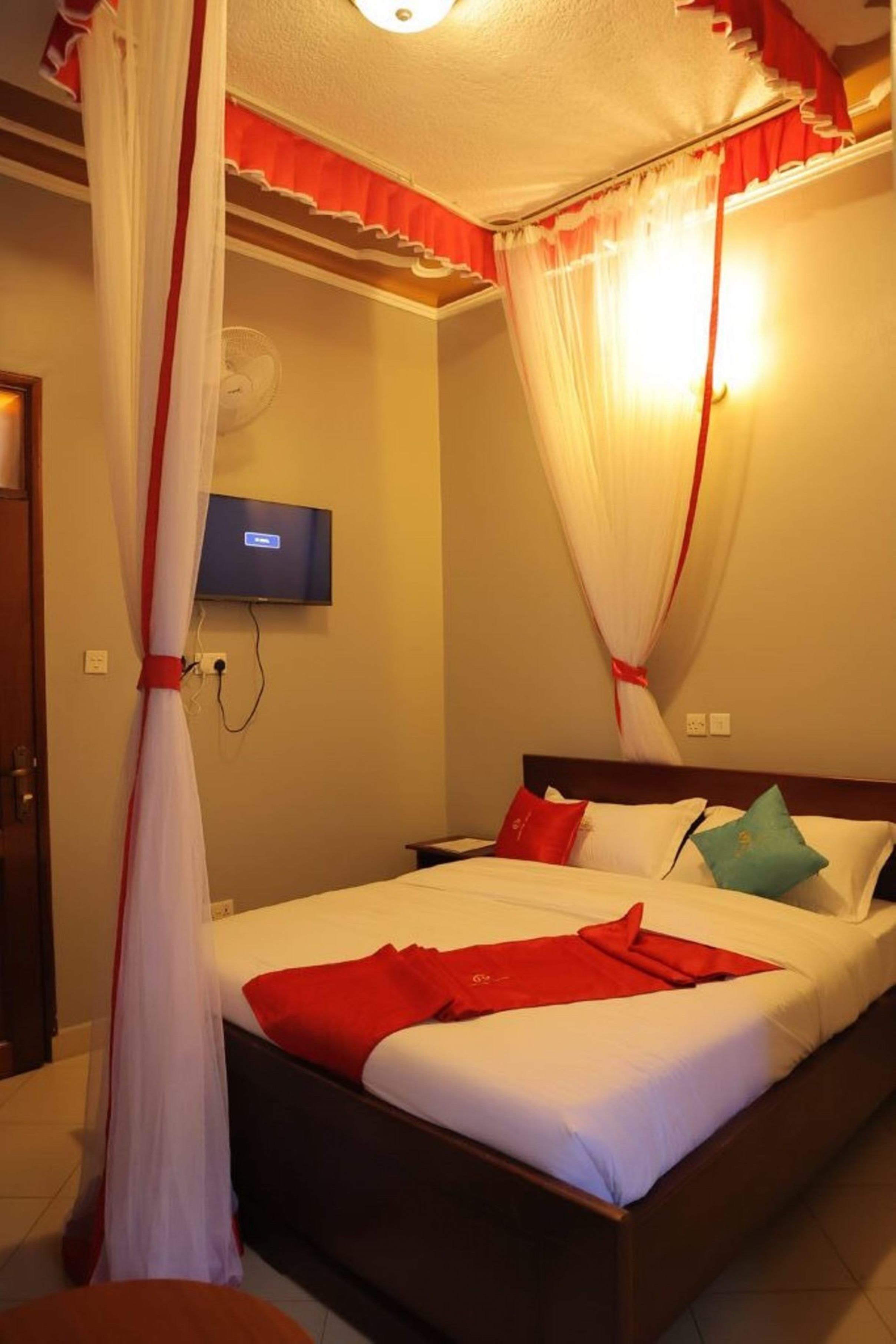 A hotel room with a bed, a TV mounted on the wall, and a mosquito net.