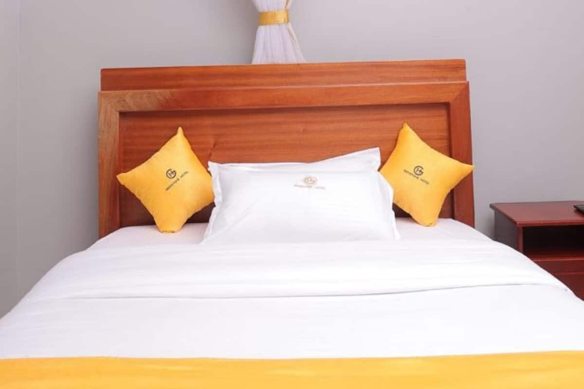 A bed with a wooden headboard, white and yellow bedding, and a canopy with a yellow trim.